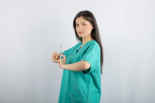 Woman doctor wearing green uniform holding syringe on white. 