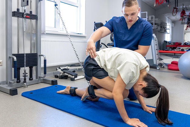 Free photo woman does legs raise exercise therapist helping with mechanical disorders