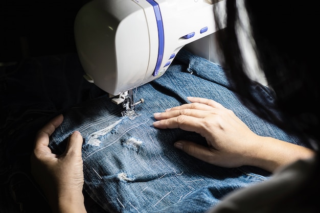 Free photo woman doing jeans patchwork using sewing machine - home diy sewing concept