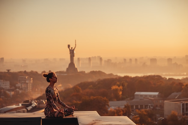 Free photo woman doing yoga on the roof of a skyscraper in big city.