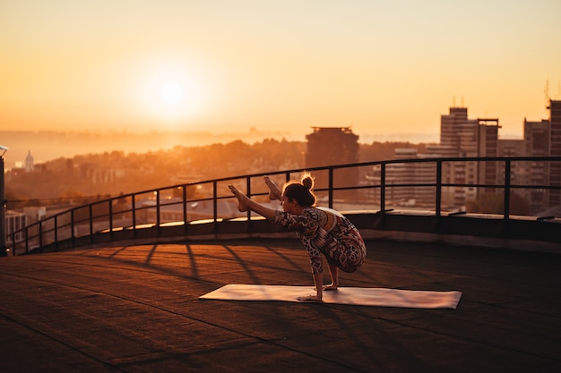 Woman doing yoga on the roof of a skyscraper in big city.