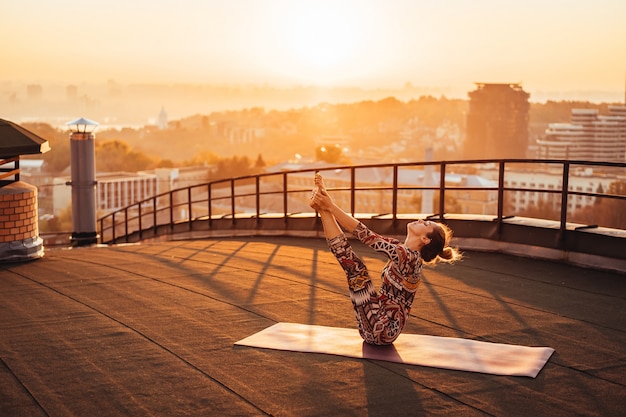 Free photo woman doing yoga on the roof of a skyscraper in big city.