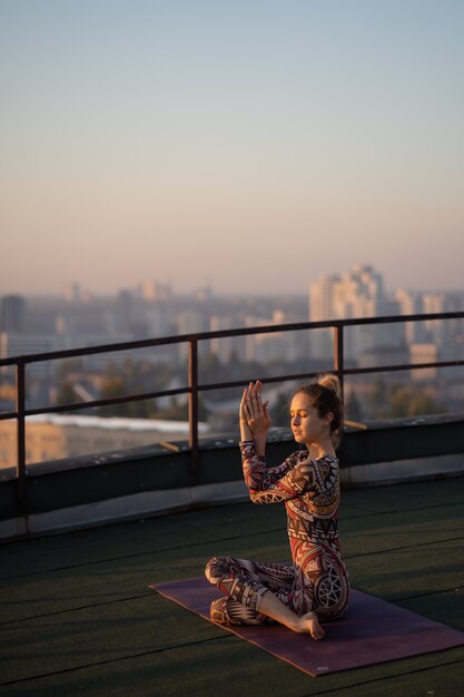 Woman doing yoga on the roof of a skyscraper in big city.