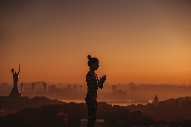 Free photo woman doing yoga on the roof of a skyscraper in big city.