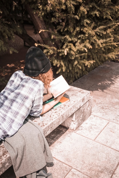 Free Photo woman dressed in plaid shirt and hat reading book in park