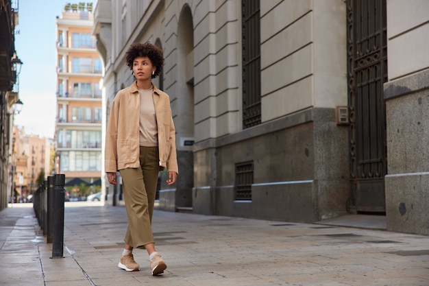 Free Photo woman dressed in trendy apparel has city tour during weekends looks away walks in downtown on pavement near ancient buildings reaches destination