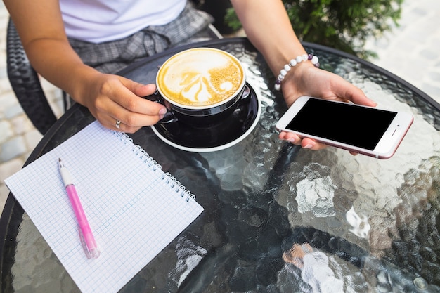 Woman drinking coffee holding smartphone