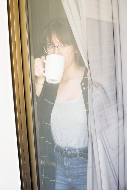 Woman drinking coffee looking through window