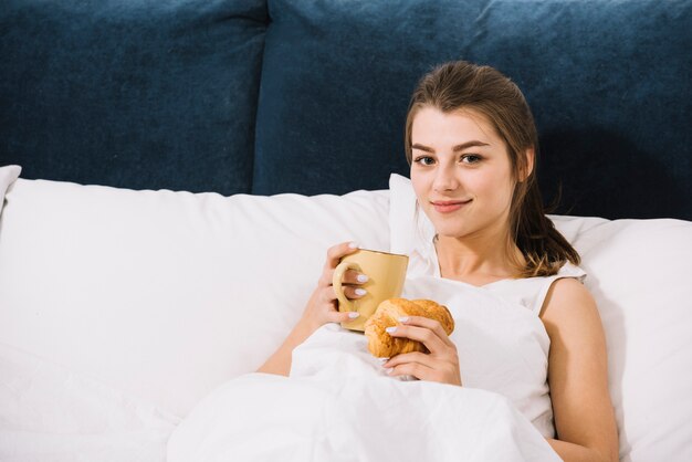 Woman drinking coffee with croissant in bed