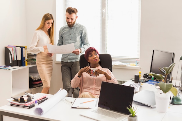 Free photo woman drinking near colleagues with blueprint