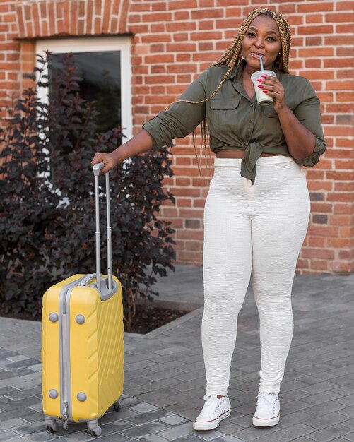 Woman drinking and standing next to her luggage