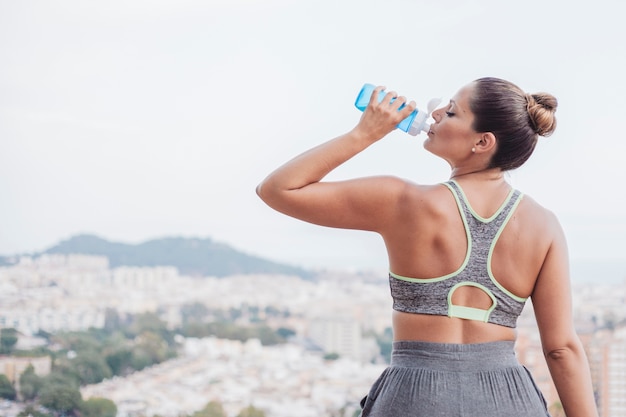 Woman drinking water in front of city