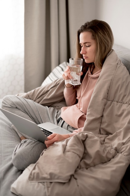 Woman drinking water and staying under blankets