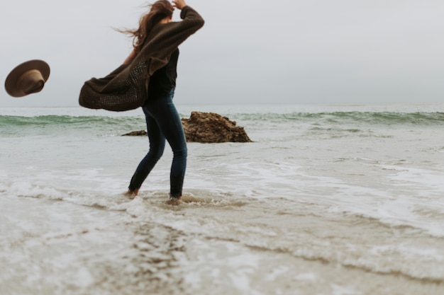 Free Photo woman dropping her hat due to the wind at the beach