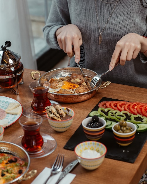 A woman eating breakfast omlette with black tea and foods around.