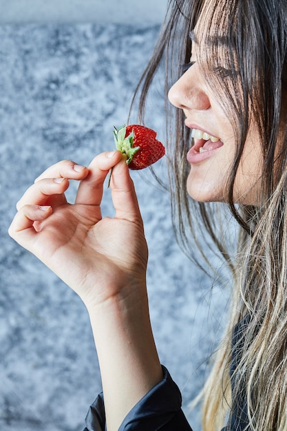 Free Photo woman eating fresh red strawberry on marble surface