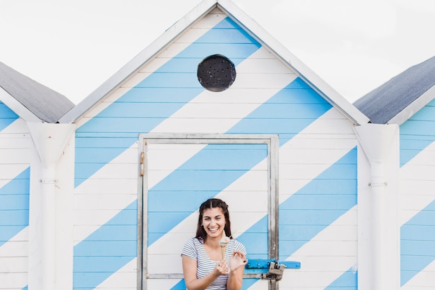 Free Photo woman eating ice cream in front of wooden house at the beach