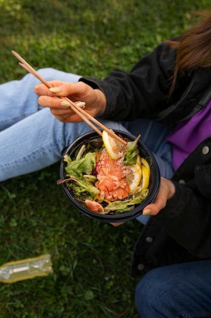 Free photo woman eating salmon dish bowl on the grass outdoors