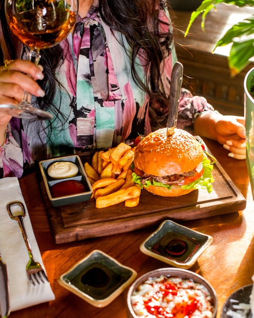 Woman eats burger served with french fries, ketchup and mayonnaise