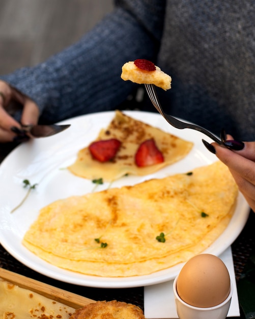 Woman eats omelet and crepe with strawberries