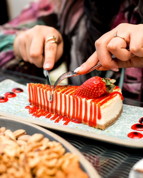 Free photo woman eats strawberry cheesecake with knife and fork