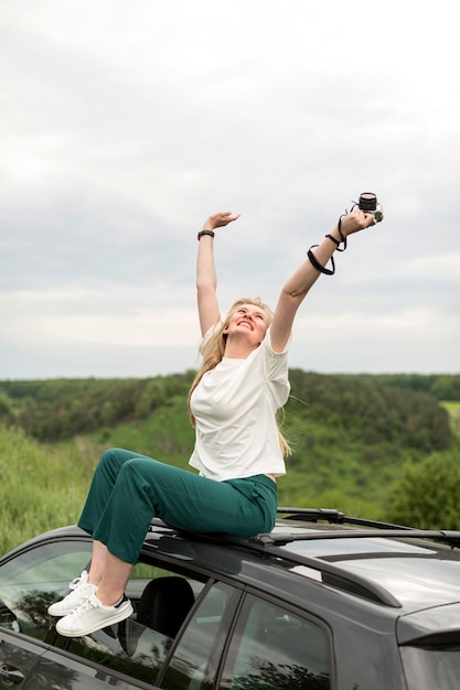 Free photo woman enjoying life while posing on top of car