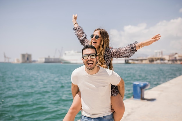 Woman enjoying piggyback ride on his boyfriend's back near the sea