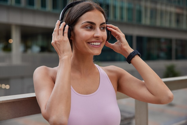 Free photo woman enjoys sport outs on wireless headphones for listening music during training wears t shirt poses outdoor on blurred