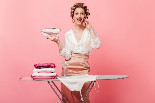 Free photo woman enthusiastically speaks on phone while ironing clothes