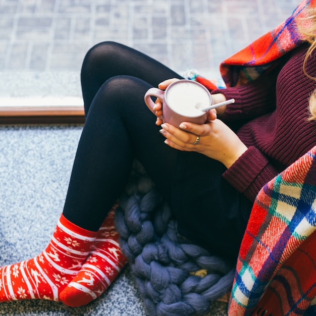 Free photo woman enveloped in plaid sits on the floor with cup of hot chocolate