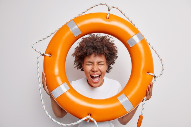 Free photo woman exclaims keeps mouth widely opened holds lifebuoy supervises people on water to prevent accident poses with lifeguard equipment on white ready to rescue you