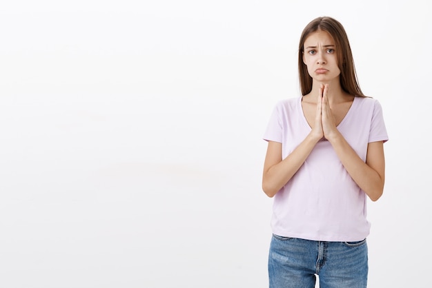 Free photo woman feeling guilty holding hands in pray pursing lips and frowning while asking forgiveness