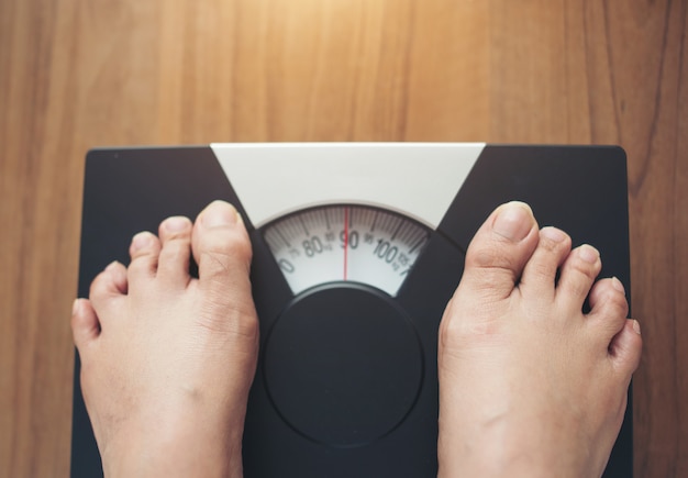 Free photo woman feet standing on weight scale on wooden background