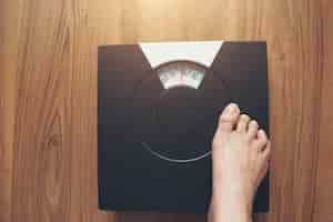 Free photo woman feet standing on weight scale on wooden background