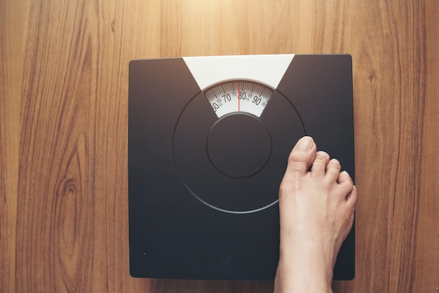 Free Photo woman feet standing on weight scale on wooden background