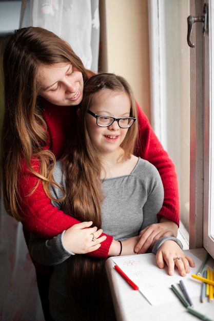 Free Photo woman and girl with down syndrome posing by window