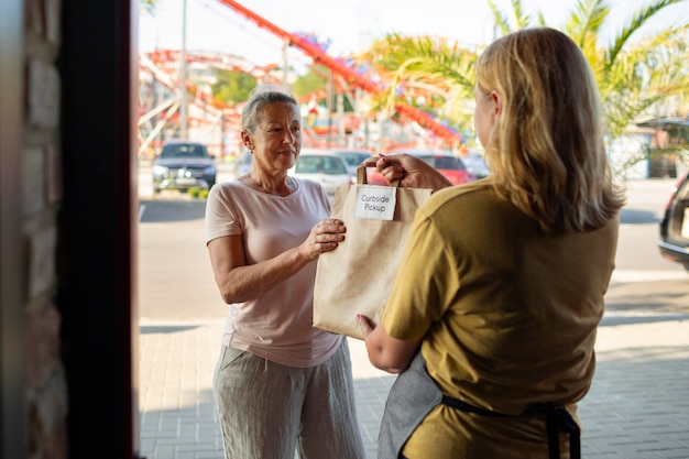 Free Photo woman giving an order to a customer at a curbside pickup outside