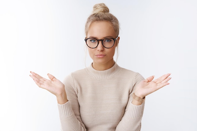 Free photo woman in glasses with bun haircut spread hands unaware and unbothered feeling careless what people thing posing self-assured