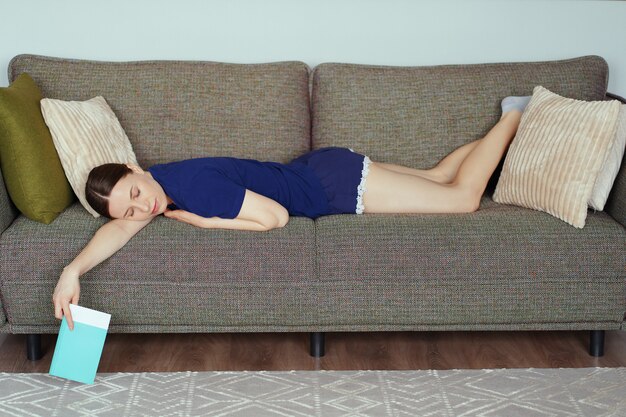 Woman got asleep while reading on sofa in the living room