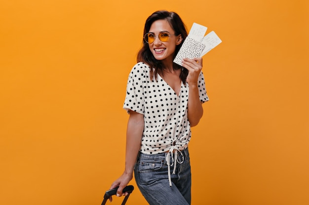 Woman in great mood poses with tickets for plane and holds suitcase