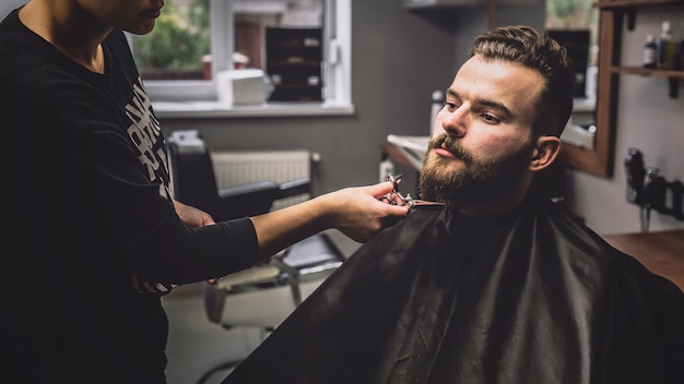 Woman grooming beard of customer with scissors