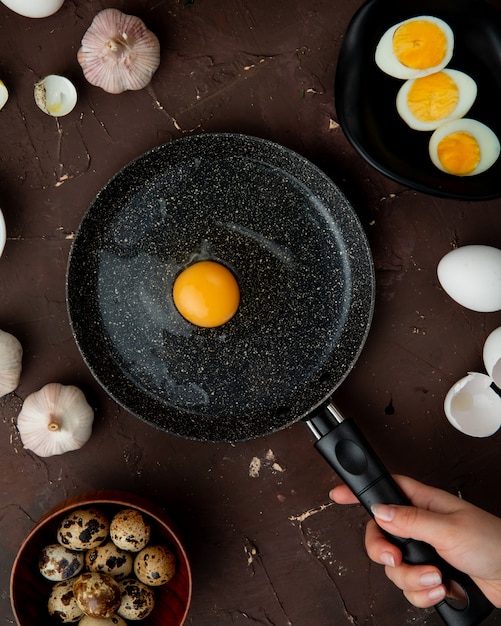 Free photo woman hand cooking egg with garlic eggs around on maroon table