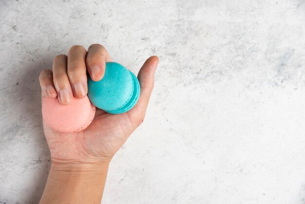 Woman hand holding two tasty macarons on marble background. 