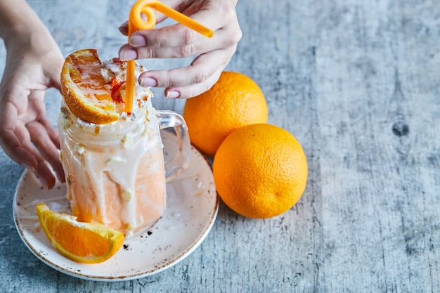 Free photo a woman hand holding a white plate with orange smoothie and slice of orange