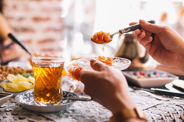 Woman hand holds a spoon and saucepan with quince jam served with tea