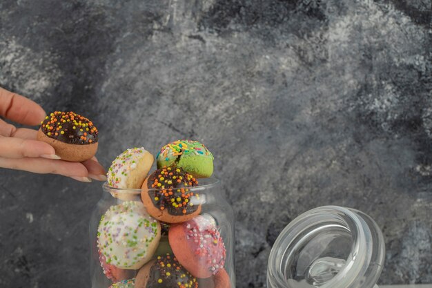 Woman hand taking a doughnut from a glass jar. 