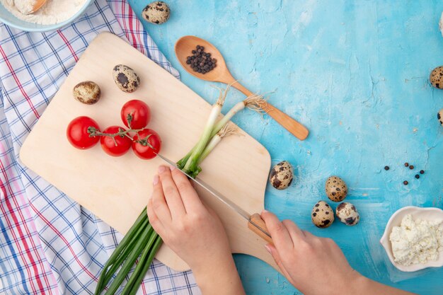 woman hands cutting scallion and other foods and vegetables on blue table