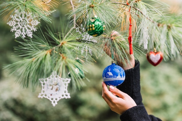 Free photo woman hands hanging christmas toys on twig in forest