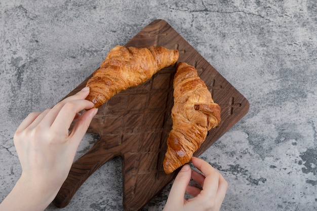 Woman hands holding fresh croissants on a wooden cutting board .