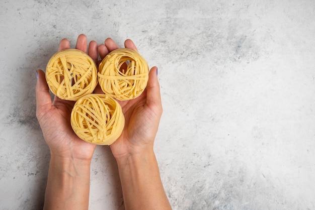 Free photo woman hands holding raw tagliatelle pasta nests on white background.